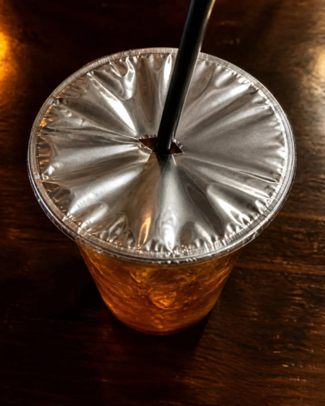 Vaso visto desde arriba con la tapa de aluminio SaftyCaps pegada y el popote atravesando el centro