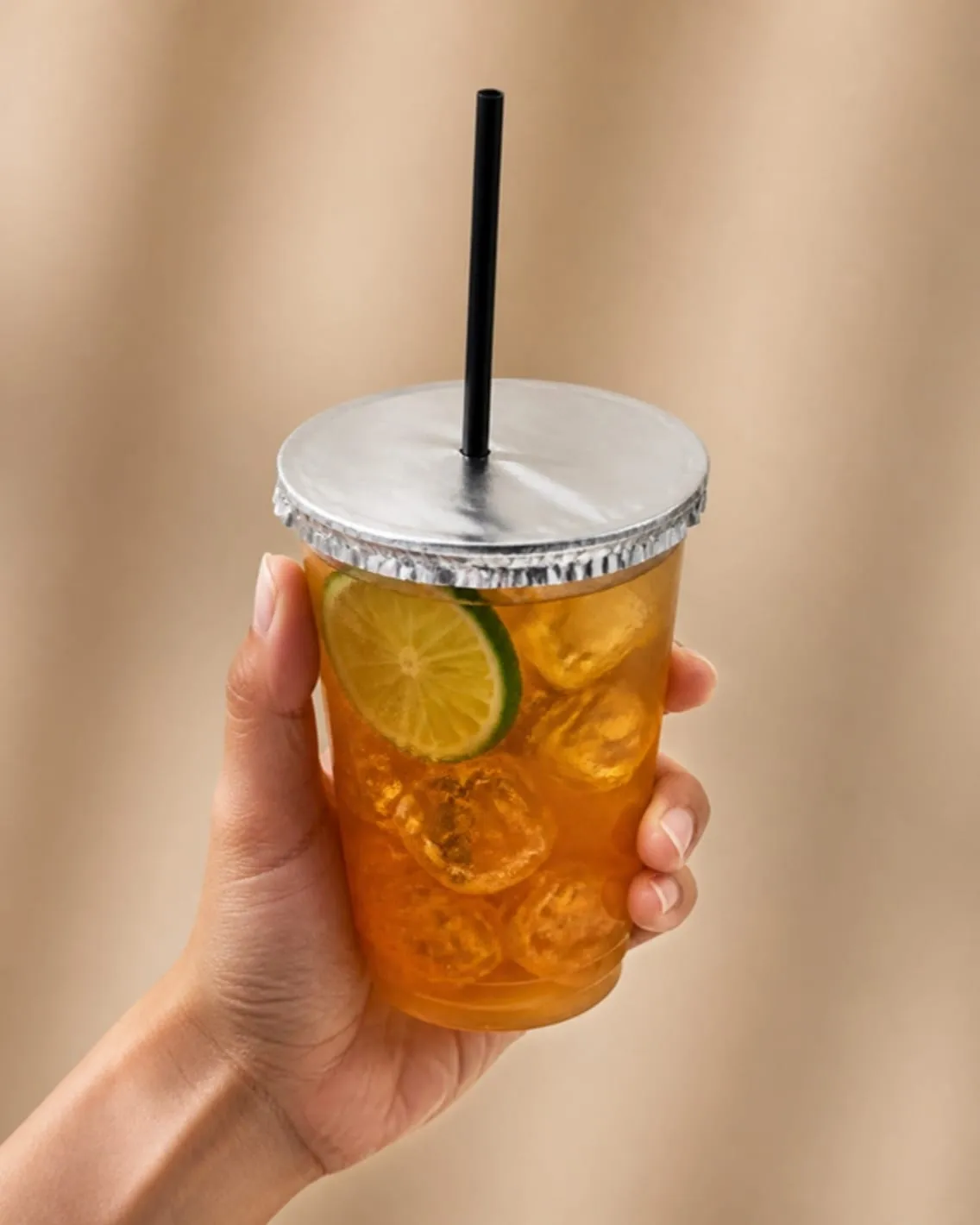 Mano sosteniendo un trago con hielo y limón, con una tapa de aluminio SaftyCaps pegada en la boca del vaso y un popote negro atravesándola